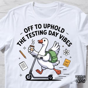 May include: White t-shirt with a cartoon goose riding a scooter, holding coffee, and wearing a backpack. The shirt features the text "OFF TO UPHOLD THE TESTING DAY VIBES" with school-themed graphics.