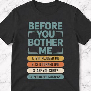 May include: Black t-shirt with the text "BEFORE YOU BOTHER ME" in teal. Below, four numbered questions in white and colored bars: "1. IS IT PLUGGED IN?", "2. IS IT TURNED ON?", "3. ARE YOU SURE?", and "4. SERIOUSLY, GO CHECK".
