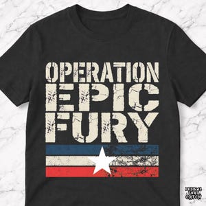 Op de afbeelding: Zwart T-shirt met de tekst "OPERATION EPIC FURY" in versleten witte letters. Daaronder een vlagafbeelding met rode, witte en blauwe strepen en een witte ster. Het T-shirt heeft een ronde hals.