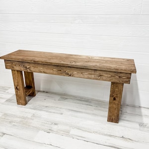 May include: A rustic wooden bench with a dark brown stain. The bench has a simple design with straight legs and a rectangular top.