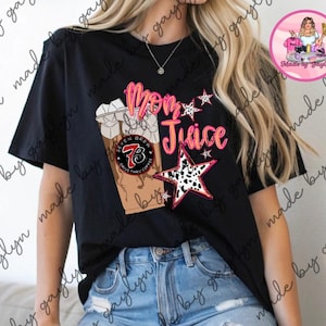 May include: Black t-shirt with a graphic design featuring the words "Mom Juice" in pink and orange, a coffee cup, and star accents. The coffee cup has the text "Seven Brew Drive Thru Coffee".