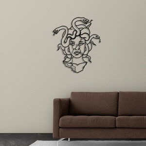 May include: Black metal wall art depicting Medusa, a Greek mythological figure with snakes for hair. The art is mounted on a white wall above a brown couch.