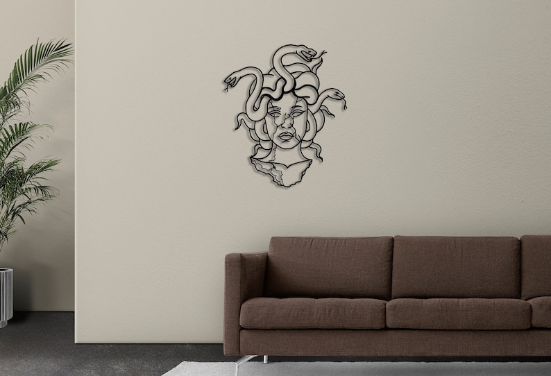 May include: Black metal wall art depicting Medusa, a Greek mythological figure with snakes for hair. The art is mounted on a white wall above a brown couch.