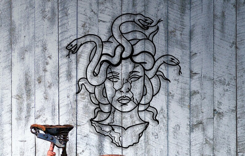 May include: Black metal wall art depicting Medusa, a mythical Greek figure with snakes for hair. The art is in a minimalist style and features a detailed face with a fierce expression.