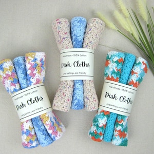 May include: Three bundles of handmade dish cloths in various colors, including blue, pink, yellow, and orange. Each bundle is wrapped with a paper label that reads "Dish Cloths" and "Handmade - 100% Cotton".