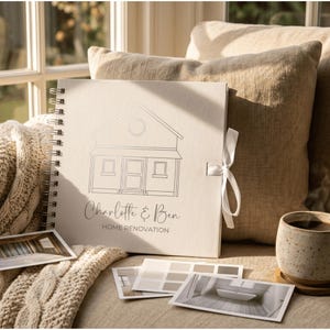 May include: A square, off-white spiral-bound scrapbook featuring a line-art illustration of a house, the text "Charlotte & Ben" in script, and "HOME RENOVATION" in block letters, secured with a white ribbon tie and accompanied by photo prints.