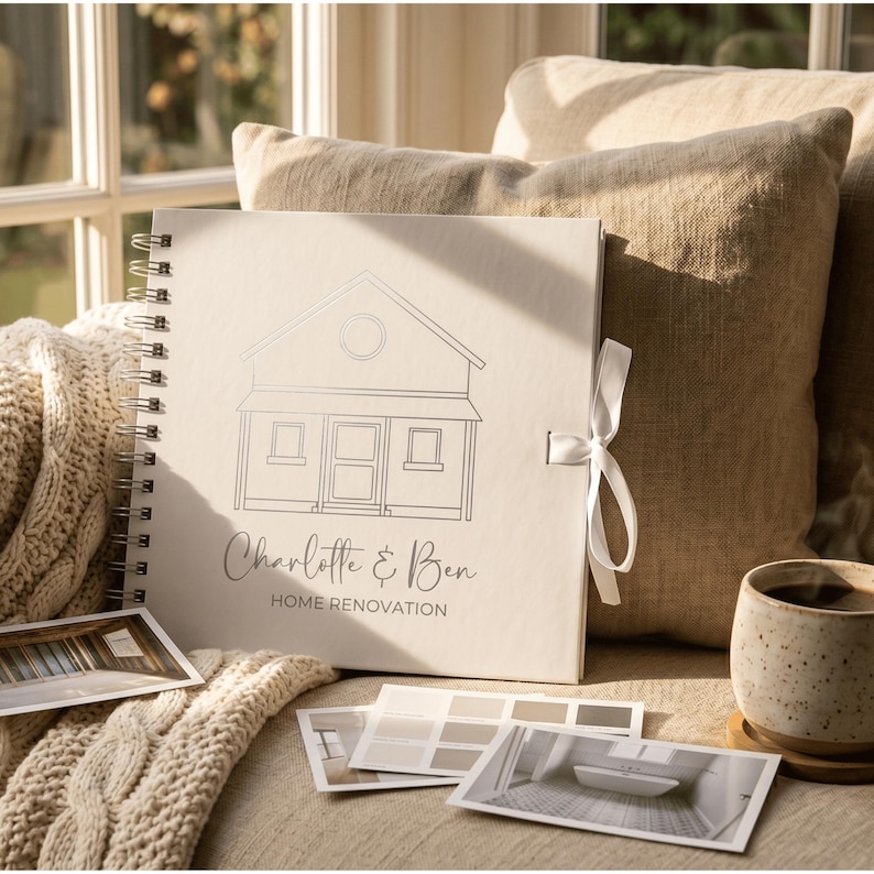 May include: A square, off-white spiral-bound scrapbook featuring a line-art illustration of a house, the text "Charlotte & Ben" in script, and "HOME RENOVATION" in block letters, secured with a white ribbon tie and accompanied by photo prints.