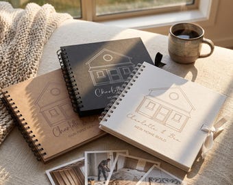 May include: Three spiral-bound square albums in tan, black, and white with house line art and text including Charlotte & Ben. The white album features a white ribbon tie. Four square photographs showing construction progress are arranged below the albums.