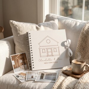 May include: A square spiral-bound scrapbook with a white cover featuring a brown line drawing of a house, the text "Charlotte & Ben" and "NEW HOME BUILD," and a white ribbon tie, accompanied by four square photographs of a home construction site.