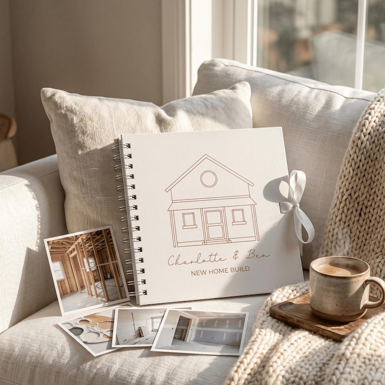 May include: A square spiral-bound scrapbook with a white cover featuring a brown line drawing of a house, the text "Charlotte & Ben" and "NEW HOME BUILD," and a white ribbon tie, accompanied by four square photographs of a home construction site.