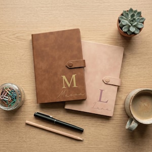 May include: Two rectangular notebooks with snap closures, one brown with the gold letter M and name Mason, one light pink with the letter L and name Luna. Includes a black pen, a wooden pencil, a jar of colourful paper clips, and a small succulent.