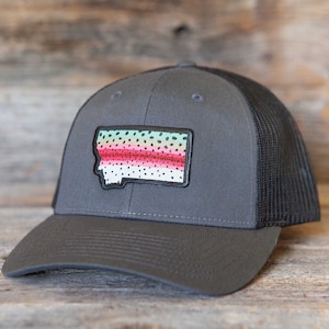 Puede incluir: Gorra de camionero gris con parte trasera de malla negra y visera curva. La gorra presenta un parche con la forma de Montana, con un diseño de trucha arcoíris colorido. Fabricada en tejido resistente, con cierre de broche ajustable.