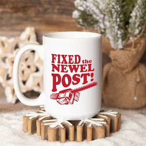 May include: White ceramic coffee mug with a red graphic that says "FIXED the NEWEL POST!" and a red illustration of a chainsaw.