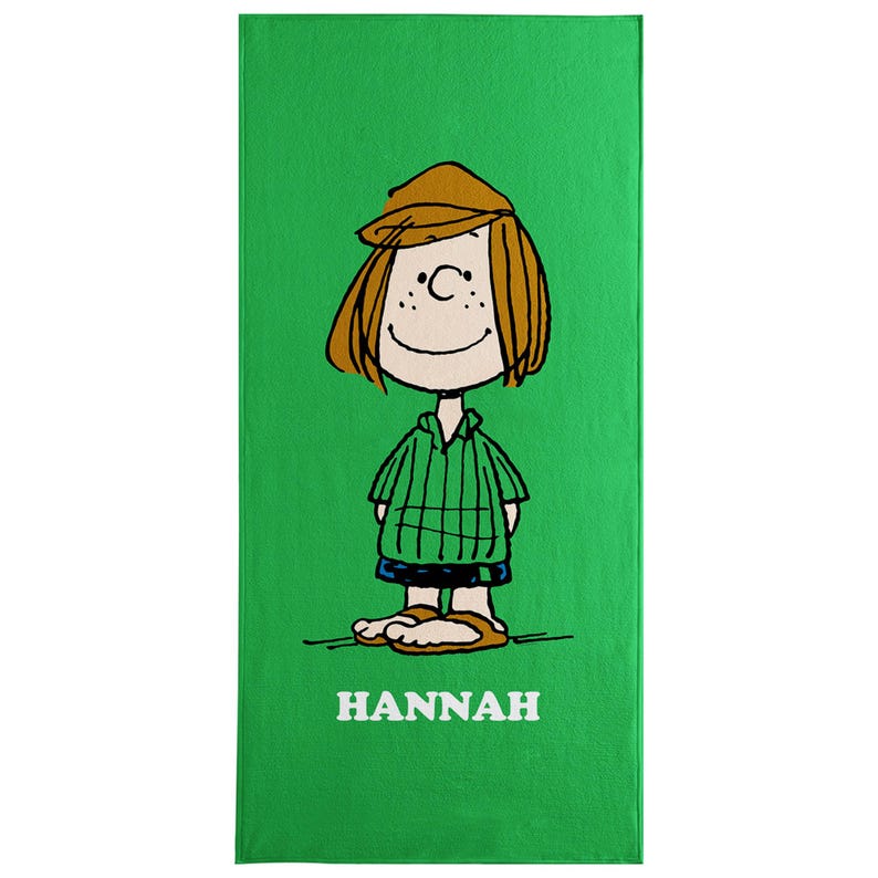 May include: A green beach towel featuring a cartoon illustration of a girl with brown hair, a brown hat, and a green striped shirt. The name "HANNAH" is printed in white at the bottom of the towel.