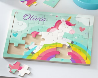 May include: A wooden puzzle featuring a white unicorn with a rainbow and stars on a light blue background. The puzzle is personalized with the name "Olivia".