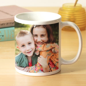 May include: White ceramic mug with a photo of two children smiling and hugging. The girl is wearing a floral dress and the boy is wearing a green shirt.