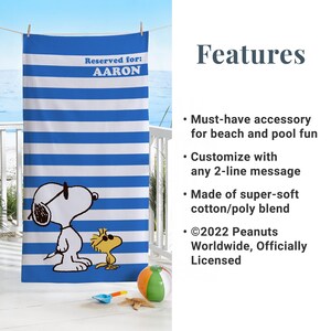 Puede incluir: Una toalla de playa a rayas azules y blancas con una imagen de dibujos animados de Snoopy con gafas de sol y Woodstock. La toalla tiene el texto "Reservado para: AARON" en la parte superior.