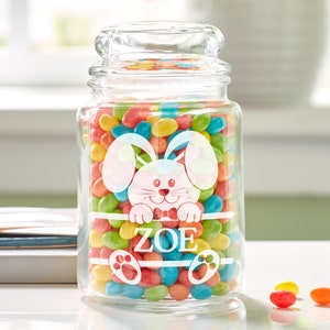 May include: A clear glass jar with a lid filled with colorful jelly beans. The jar has a white bunny design with a bow tie and the name "ZOE" etched on the front.