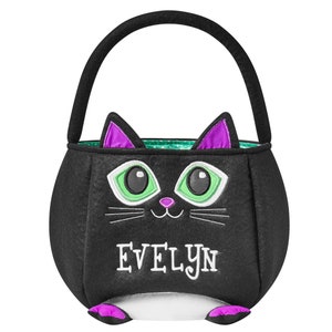May include: Black felt Halloween trick-or-treat bag shaped like a cat. The bag has a black handle and features a cat face with green eyes, purple ears, and the name "EVELYN" embroidered in white. The interior has a green and white polka dot pattern.