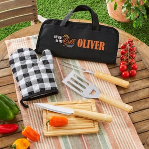 May include: A black and white checkered oven mitt, a wooden cutting board with a knife, a spatula, a grilling fork, and a black carrying case with the text "All Up In My Grill OLIVER".