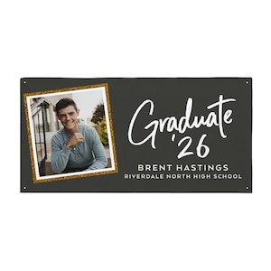 May include: A dark gray graduation banner with a photo of a graduate in a gold glitter frame. The banner reads "Graduate '26" in white script, along with the graduate's name and high school.