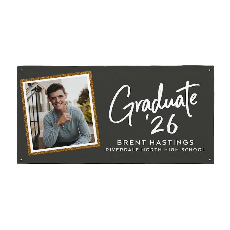 May include: A dark gray graduation banner with a photo of a graduate in a gold glitter frame. The banner reads "Graduate '26" in white script, along with the graduate's name and high school.
