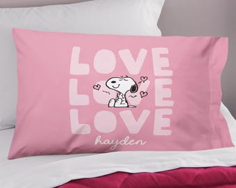 Peut inclure: Taie d'oreiller rose avec le mot "LOVE" en lettres blanches, un motif Snoopy et le nom "hayden" en écriture cursive. Le motif Snoopy montre Snoopy assis avec des cœurs.