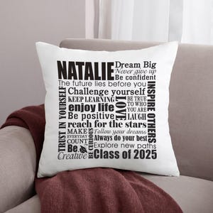 May include: White cushion with black text that reads "Natalie Class of 2025" and includes words of encouragement and inspiration, such as "Dream Big", "Never Give Up", "Be Confident", "Challenge Yourself", "Keep Learning", "Enjoy Life", "Be Positive", "Reach for the Stars", "Inspire Others", "Trust in Yourself", "Be True to Who You Are", "Make Everyday Count", "Follow Your Dreams", "Always Do Your Best", "Be Curious", "Explore New Paths", and "Be Creative".
