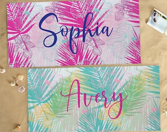 May include: Two beach towels with tropical floral patterns. The top towel is pink with white and blue floral designs and the text "Sophia". The bottom towel is turquoise with white and yellow floral designs and the text "Avery".