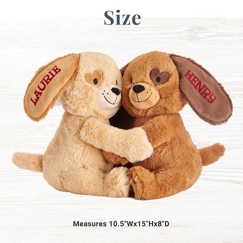 May include: Two plush brown and tan dog toys hugging each other. The dogs have embroidered hearts on their eyes and the names "Laurie" and "Henry" on their ears. The toys measure 10.5 inches wide by 15 inches tall by 8 inches deep.