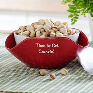 May include: Red and white ceramic bowl with a white inner bowl. The bowl is filled with pistachios and has the text "Time to Get Crackin'" printed on the outside.