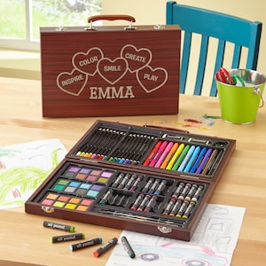 May include: A wooden art case with a personalized inscription "EMMA" and hearts with words "INSPIRE", "COLOR", "SMILE", "CREATE", and "PLAY". The case is open and contains a variety of art supplies, including colored pencils, markers, crayons, oil pastels, and watercolor paints.