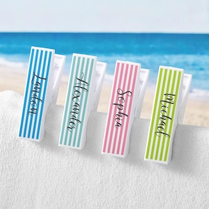 May include: Four plastic towel clips featuring vertical stripes in blue, light blue, pink, and lime green. Each clip is personalized with a black script name: Landon, Alexander, Sophia, and Michael, printed vertically on the front surface.