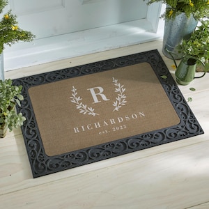 May include: A rectangular doormat with a dark gray, ornate border. The center has a tan background with the letter "R" inside a laurel wreath, the name "RICHARDSON", and the year "est. 2023" in white.
