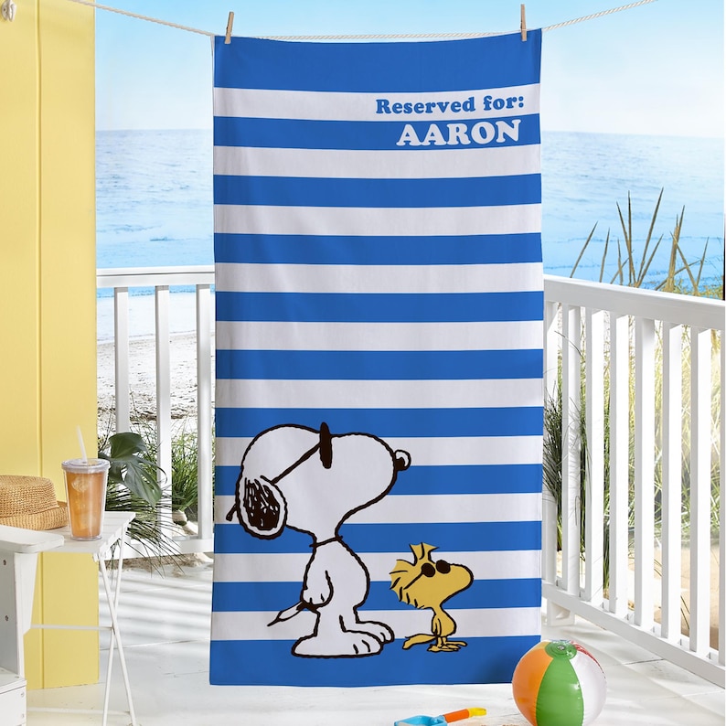 Puede incluir: Toalla de playa a rayas azules y blancas con Snoopy y Woodstock con gafas de sol. La toalla dice "Reservado para: AARON".