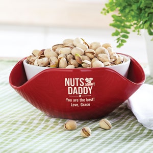 May include: Red ceramic bowl with a white inner bowl, filled with pistachios. The bowl has the text "NUTS about DADDY" and "You are the best! Love, Grace" printed on it.