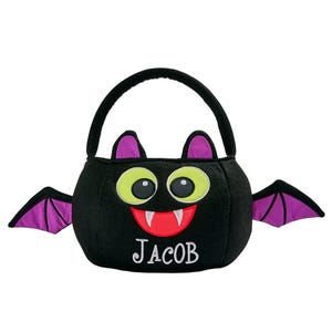 May include: A black Halloween treat bag shaped like a bat, with a handle and wings. The bat has large green eyes, a red mouth with white fangs, and the name "JACOB" embroidered in white.