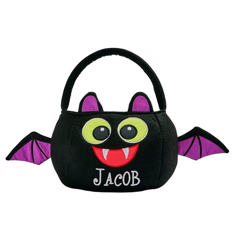 May include: A black Halloween treat bag shaped like a bat, with a handle and wings. The bat has large green eyes, a red mouth with white fangs, and the name "JACOB" embroidered in white.