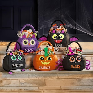 May include: Five Halloween-themed treat bags in the shape of an owl, bat, cat, pumpkin, and spider. Each bag is black, orange, or purple, with embroidered names and cartoon faces. The bags are filled with wrapped candies and treats.