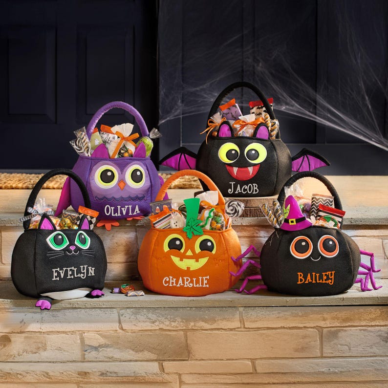 May include: Five Halloween-themed treat bags in the shape of an owl, bat, cat, pumpkin, and spider. Each bag is black, orange, or purple, with embroidered names and cartoon faces. The bags are filled with wrapped candies and treats.