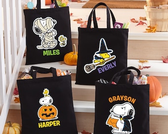 May include: Four black Halloween tote bags with different Snoopy and Woodstock designs. One bag features Snoopy as a mummy with the name "MILES". Another shows Woodstock as a witch with the name "EVERLY". A third bag has Snoopy on a pumpkin with "HARPER". The last bag has Snoopy as a vampire with "GRAYSON".