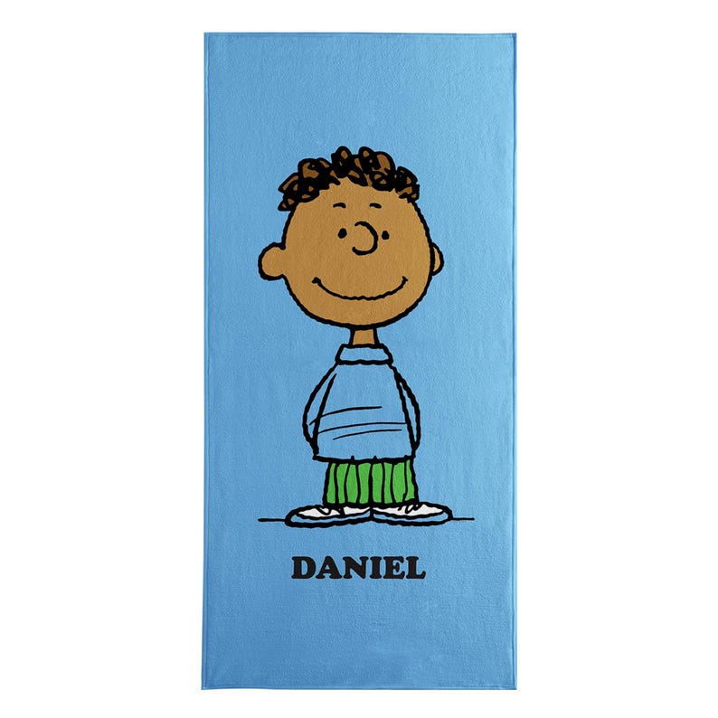 May include: A light blue rectangular towel featuring a cartoon illustration of a boy with brown skin, black curly hair, and a smiling face. He wears a blue shirt and green pants. The name "DANIEL" is printed in black at the bottom.
