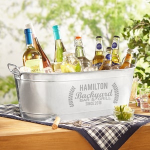 May include: A silver galvanized metal tub filled with ice and bottles of wine and beer. The tub has a personalized inscription that reads "Hamilton Backyard Bar & Grill Since 2016".