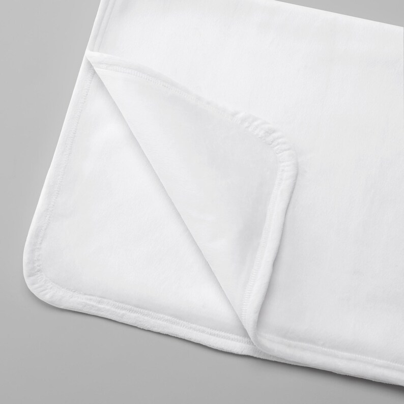 May include: A solid white rectangular blanket featuring a soft, plush texture and finished with neatly stitched rounded corners. The fabric is folded over at one corner to reveal the consistent white color on both the top and underside surfaces.