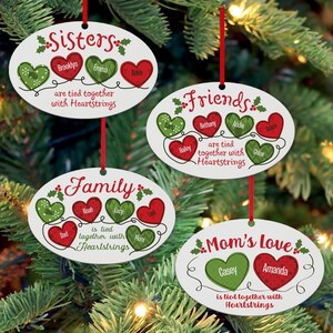 May include: Four oval-shaped Christmas ornaments with red and green hearts and names on each. The ornaments read "Sisters", "Family", "Friends", and "Mom's Love". Each ornament has the phrase "are tied together with Heartstrings".