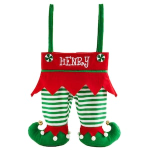 May include: A Christmas stocking shaped like elf legs. The red top has the name "HENRY" embroidered in white. The legs are green and white striped, with green elf shoes and jingle bells.