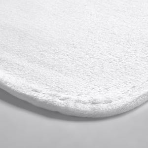 May include: A solid white bath mat featuring a soft, plush, and textured fabric surface with rounded corners and a stitched hem along the edge. The material has a dense, short-pile construction that creates a uniform and clean appearance.