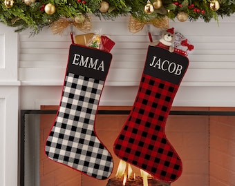 May include: Two personalized Christmas stockings with red and black buffalo plaid patterns. The stocking on the left is black and white with the name "EMMA" embroidered on it. The stocking on the right is red and black with the name "JACOB" embroidered on it.