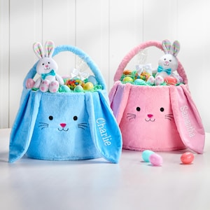 May include: Two plush bunny-shaped Easter baskets, one blue and one pink, filled with candy and eggs. The blue basket has the name "Charlie" embroidered on it, and the pink basket has the name "Samantha" embroidered on it.
