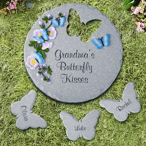 May include: A set of three gray stone butterfly garden stepping stones. The center stone features a butterfly cutout and the text "Grandma's Butterfly Kisses". The other two stones have the names "Olivia" and "Rachel" inscribed on them.